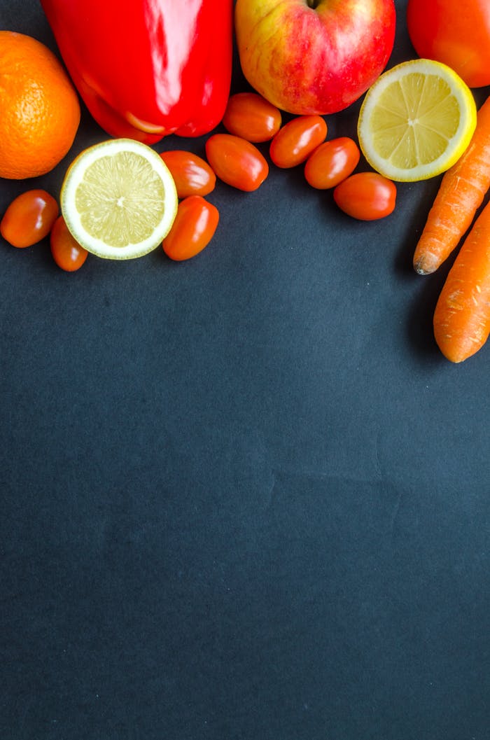 Colorful arrangement of fresh produce including citrus, carrots, and tomatoes on a dark backdrop.